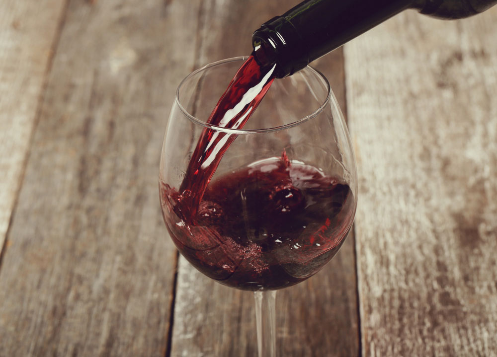 Weinglas, in das aus einer Flasche Rotwein gefüllt wird